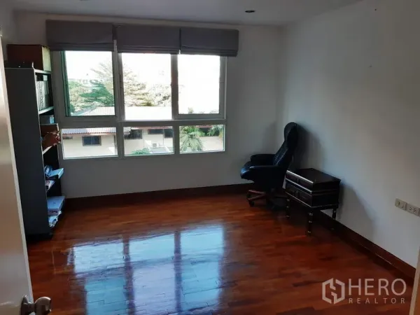 公寓 出售在Watthana, Bangkok - 宽敞房间，亮面木地板与大窗，带书架和椅子。