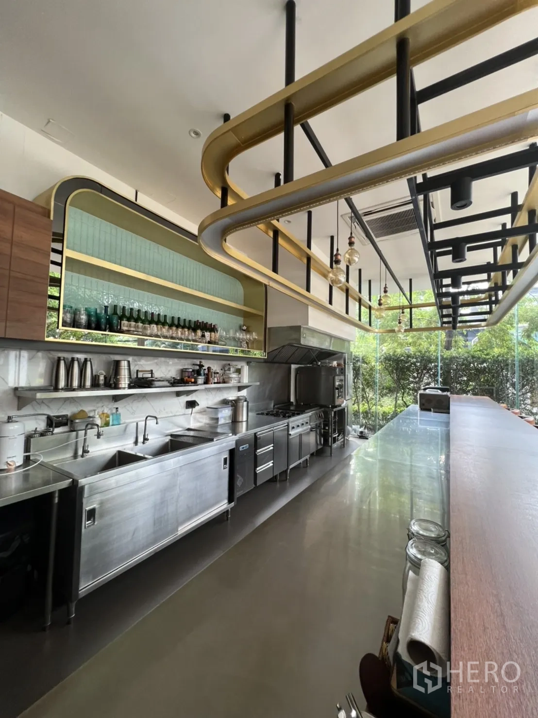零售空间 出租在Watthana, Bangkok - 不锈钢商用厨房一线设备，带水槽、烤箱、炉灶与置物架，外望绿景。