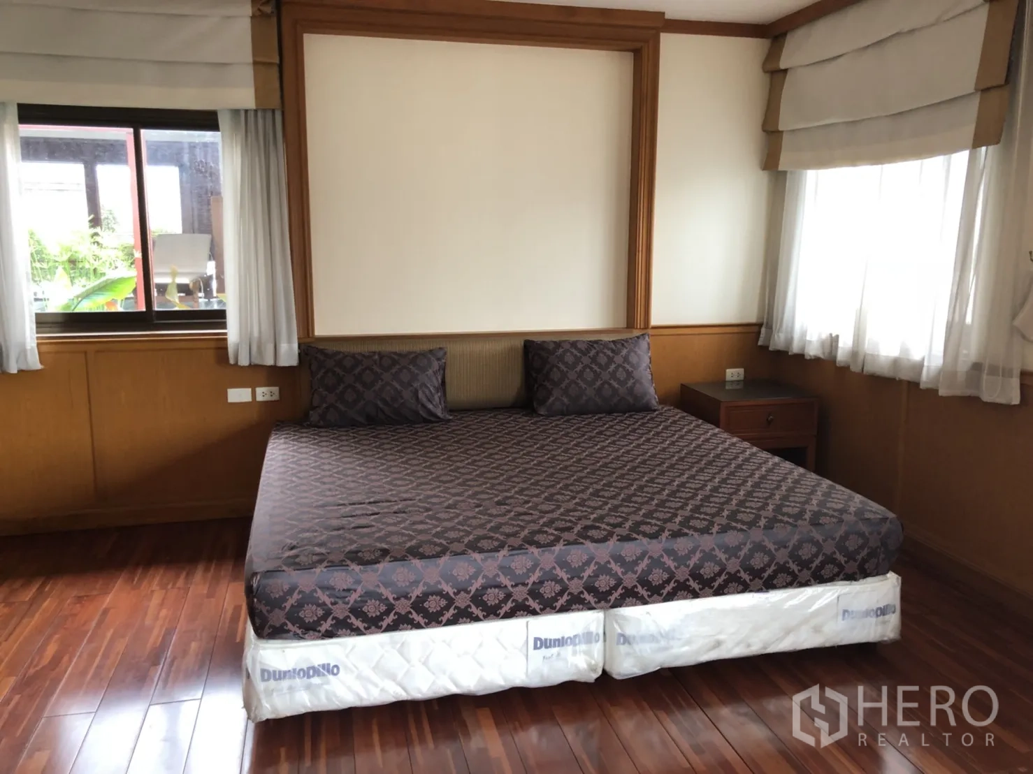 Apartment for rent in Bang Rak, Bangkok - Spacious master bedroom with large bed, wood paneling, multiple windows and polished wooden flooring.