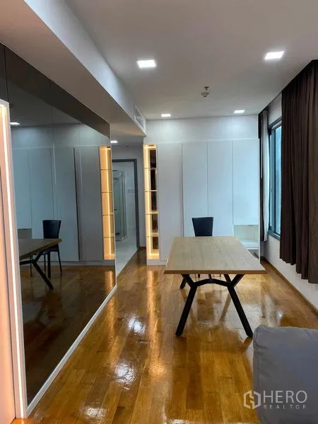 Condominium for rent or sale in Khlong Toei, Bangkok - Dining nook with wood table, full-height mirrors, wide window and warm accent lighting.