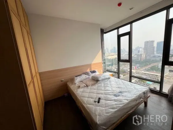 Condominium for rent in Ratchathewi, Bangkok - Primary bedroom with large windows, built-in wardrobe and panoramic skyline outlook.