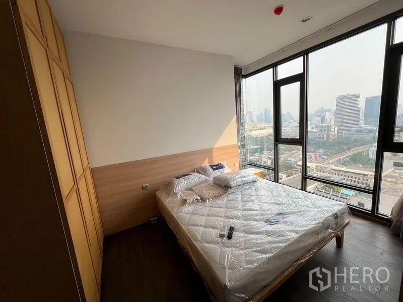 Condominium for rent in Ratchathewi, Bangkok - Primary bedroom with large windows, built-in wardrobe and panoramic skyline outlook.