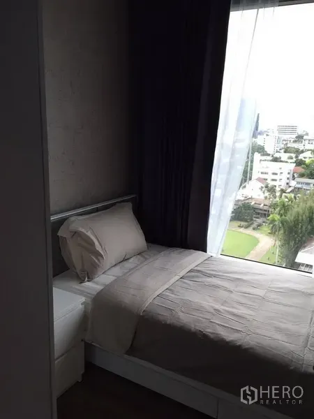 Condominium for rent in Watthana, Bangkok - Second bedroom with a single bed beside a large window overlooking the Ekkamai neighborhood.