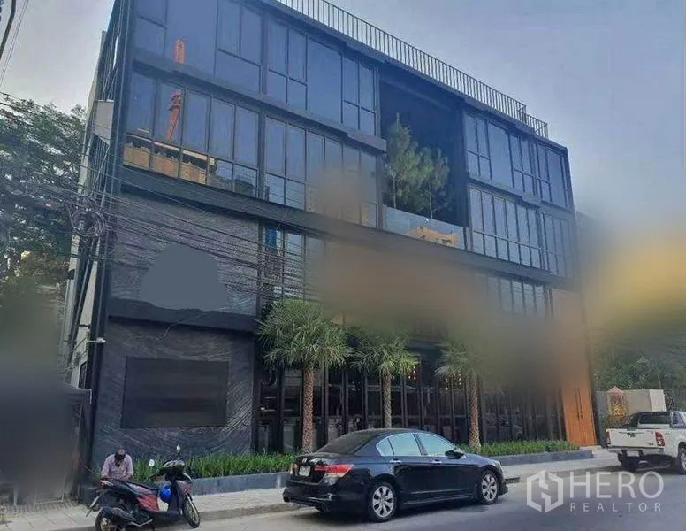 Retail Space for rent in Watthana, Bangkok - Daytime street view of a modern low-rise commercial building with palm trees and parking.