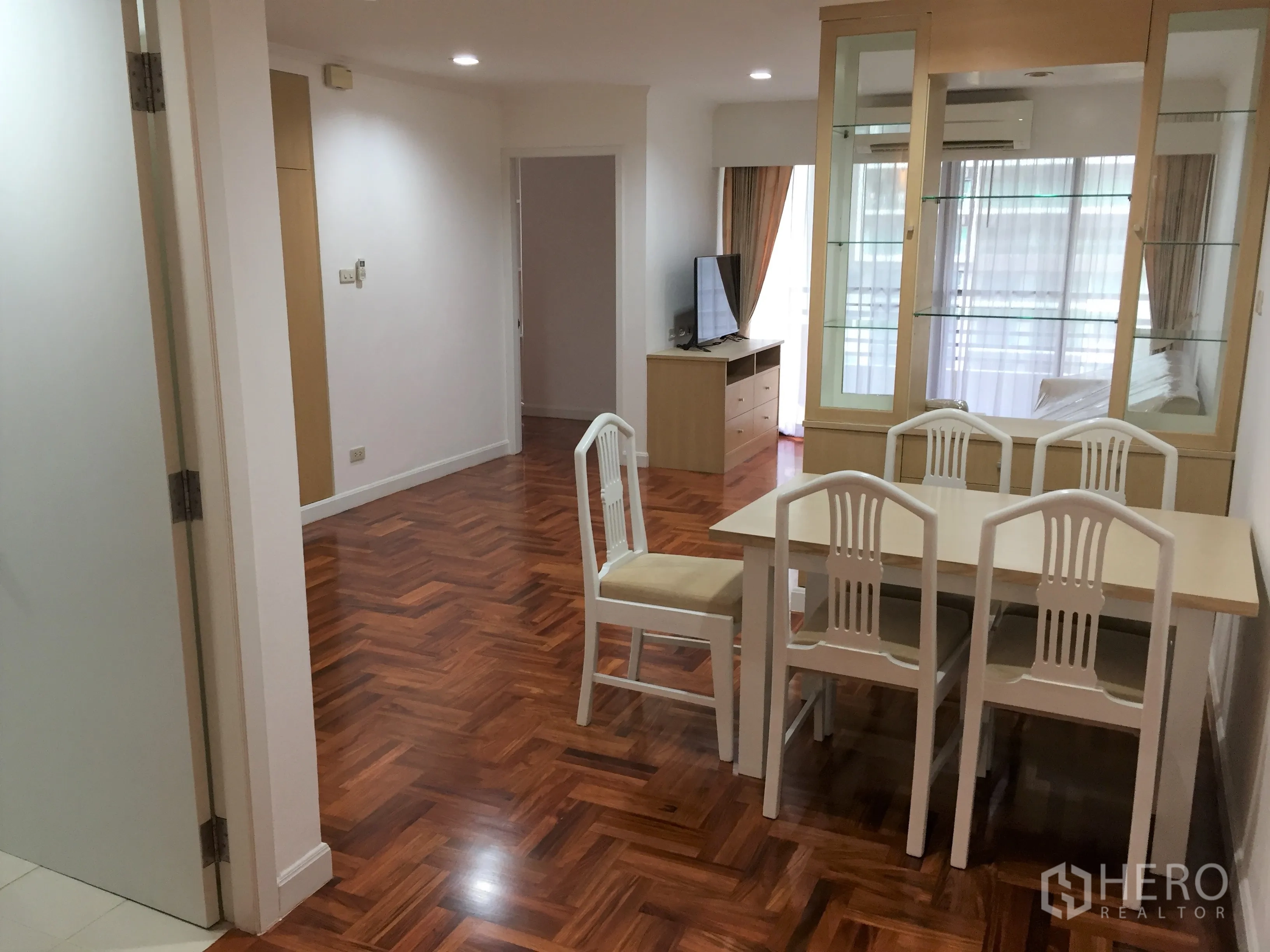 公寓 出租在Watthana, Bangkok - 餐厅四人餐桌，玻璃柜隔断，电视柜及带窗帘的阳台门。