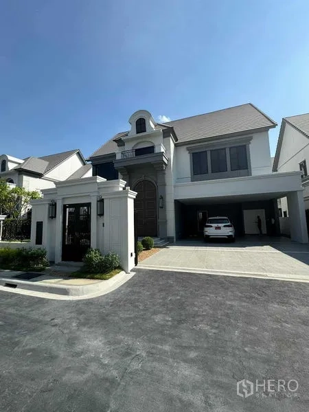 Detached House for rent in Bang Khen, Bangkok - Gated frontage and driveway leading to a modern two-storey home with covered parking in an upscale estate.
