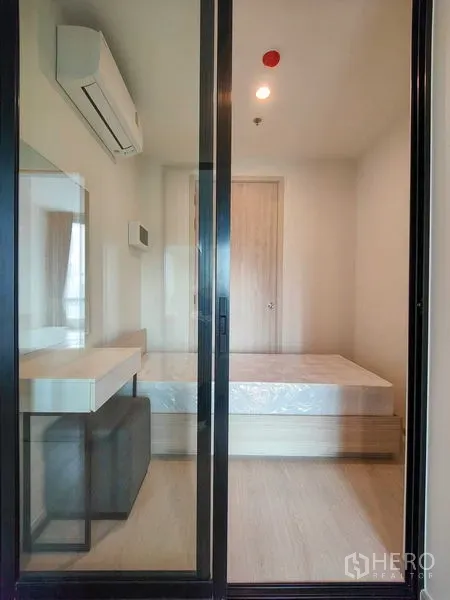คอนโด ให้เช่า - ห้องนอนขนาดกะทัดรัดหลังประตูกระจกบานเลื่อน มีฐานเตียง โต๊ะเครื่องแป้ง และแอร์แขวนผนัง