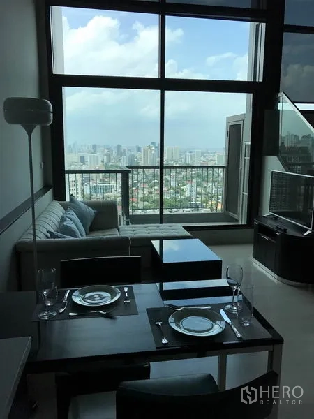 Condominium for rent in Khlong Toei, Bangkok - Double-height living and dining area with floor-to-ceiling windows, balcony, and skyline view in a Khlong Toei condo.