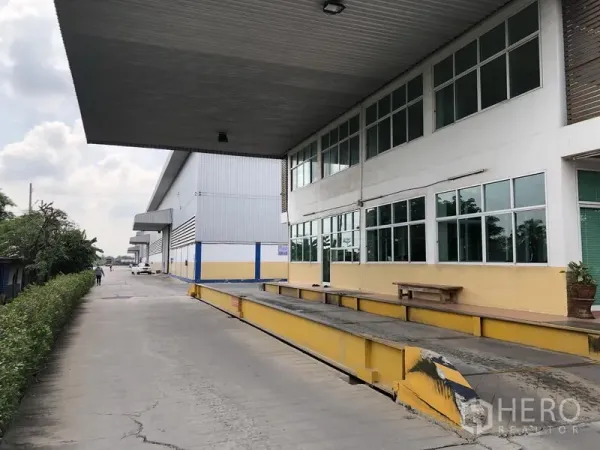 Warehouse for rent in Phra Nakhon Si Ayutthaya - Covered loading dock beside a glass-front office wing and landscaped verge.