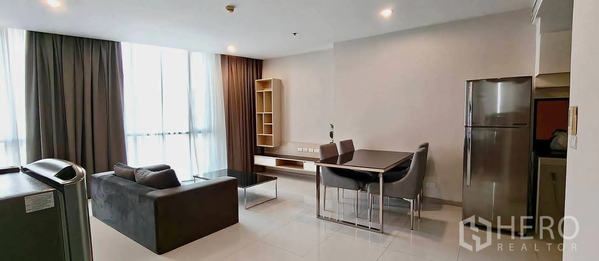 公寓 for rent in Watthana, Bangkok - 客厅采光充足，落地窗与深色窗帘相配，旁为餐区与冰箱。