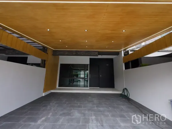 Townhouse for rent or sale in Lat Phrao, Bangkok - Carport featuring warm wood ceiling with downlights and tiled driveway.