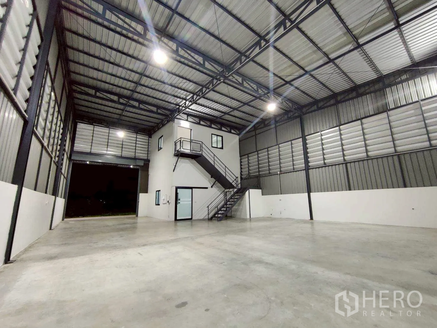 Warehouse for rent in Lam Luk Ka, Pathum Thani - Spacious high-bay warehouse interior with steel truss roof, mezzanine office box, and open roller door.