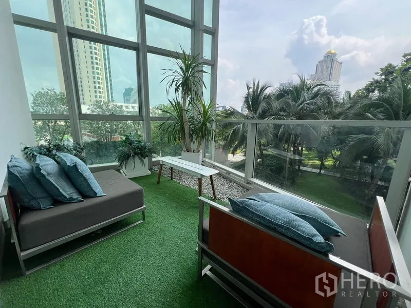 Condominium for sale in Khlong San, Bangkok - Enclosed balcony with artificial grass, lounge benches, and tropical city views.