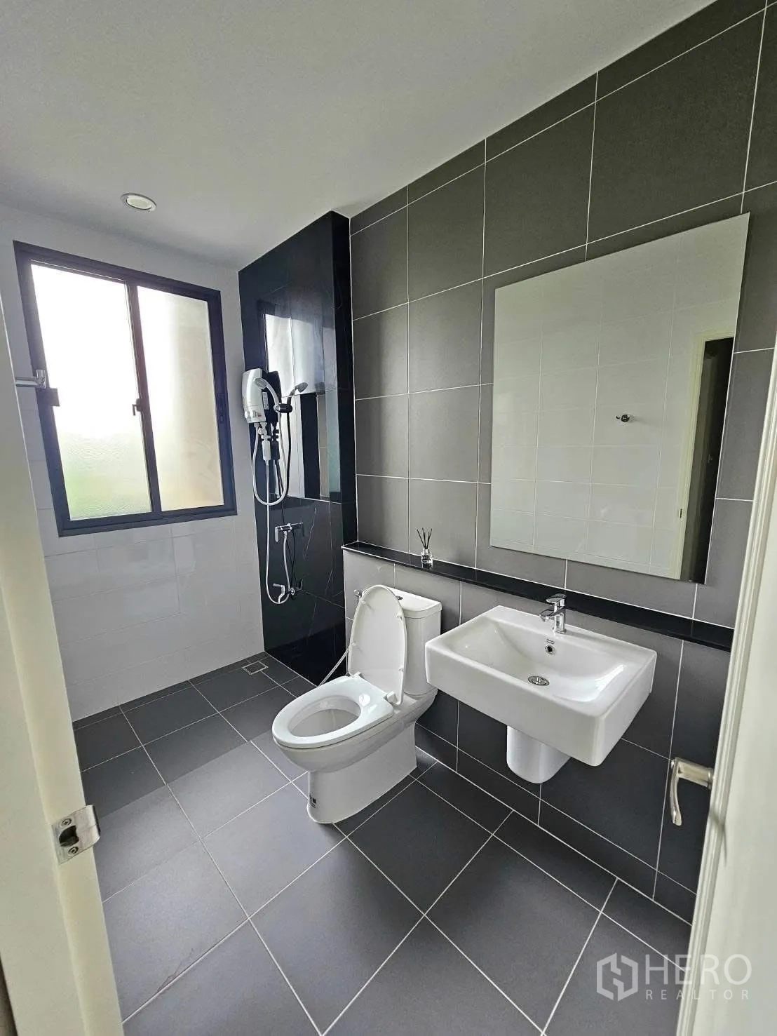 Townhouse for rent in Saphan Sung, Bangkok - Modern bathroom with gray tiles, toilet, wall mirror, and separate shower zone.