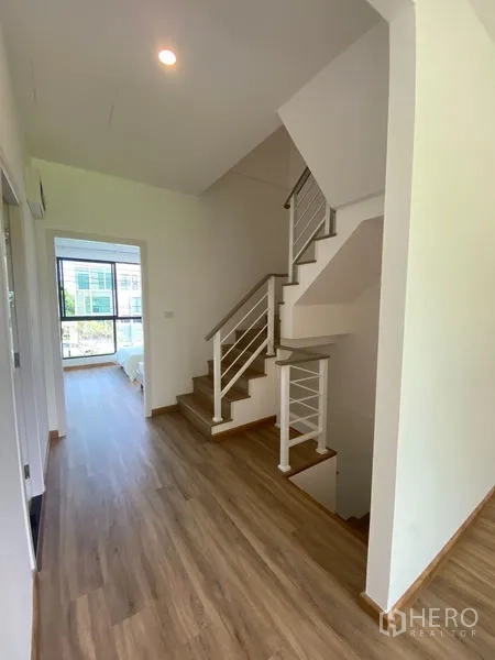 Townhouse for rent in Bang Kapi, Bangkok - Hallway with wooden staircase and metal handrail leading to sunlit bedroom.