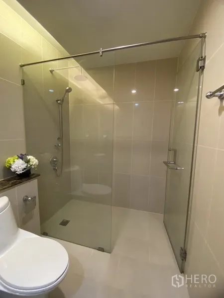 公寓 出租在Watthana, Bangkok - 现代卫浴，透明玻璃淋浴间、手持花洒与坐便器，米色瓷砖。