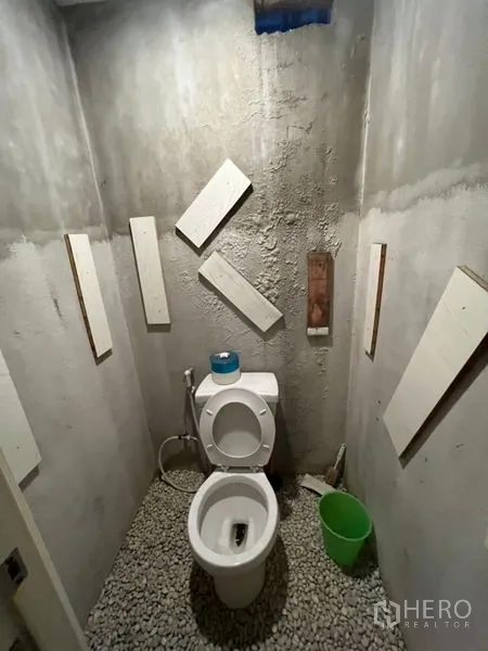 Shophouse for rent or sale in Watthana, Bangkok - Toilet cubicle with raw concrete wall texture and pebble floor.