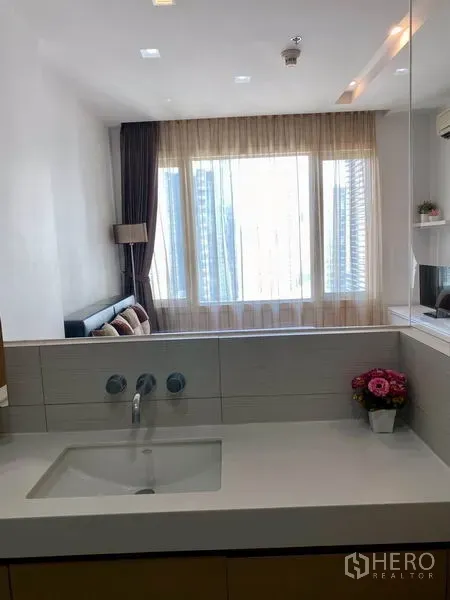 Condominium for rent in Khlong Toei, Bangkok - Modern bathroom vanity with wide mirror looking through to a windowed living area.