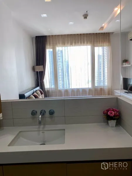 Condominium for rent in Khlong Toei, Bangkok - Modern bathroom vanity with wide mirror looking through to a windowed living area.