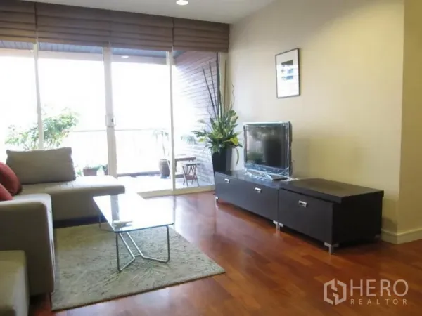 Condominium for rent in Khlong Toei, Bangkok - Bright living room with TV console and sliding glass doors leading to a balcony with plants.
