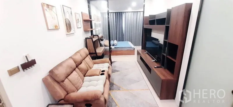Condominium for rent or sale in Huai Khwang, Bangkok - Cozy living room with recliner sofa and TV wall unit facing the bedroom.