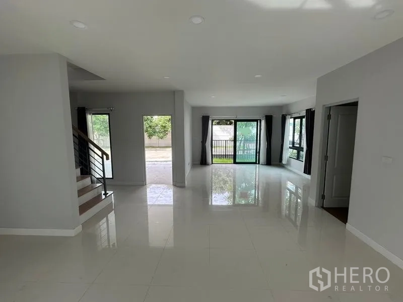 Detached House for sale in Nonthaburi - Open-plan living space with staircase and sliding glass doors to the yard.
