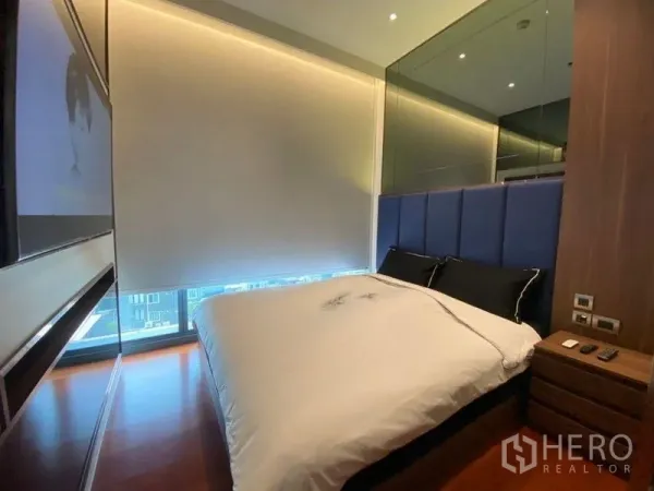 公寓 出租或出售在Watthana, Bangkok - 卧室配蓝色软包床头、遮光卷帘与镜面墙，温润木地板。