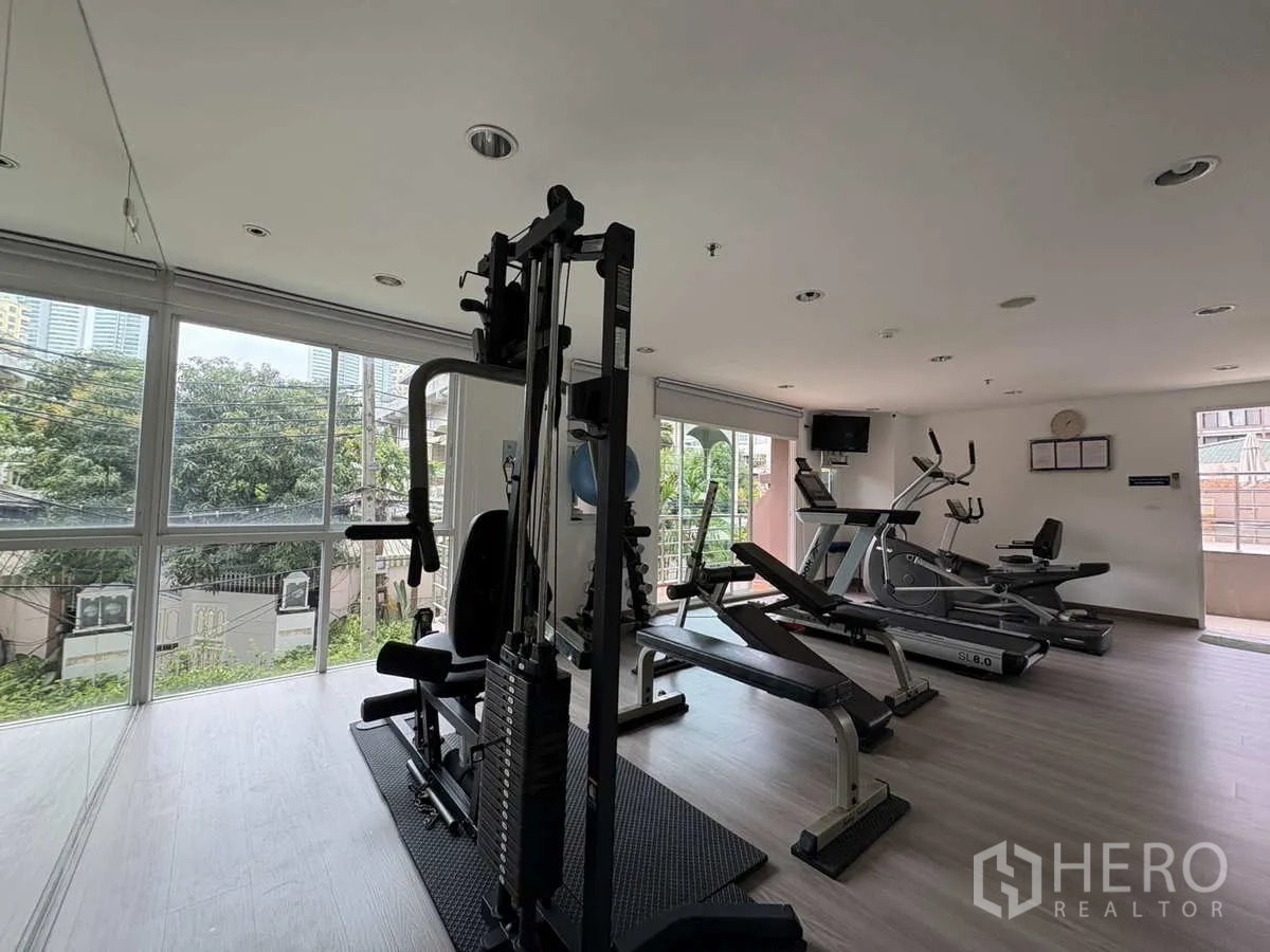 Condominium for rent in Khlong Toei, Bangkok - Fitness room with weight and cardio machines beside wide city‑view windows.