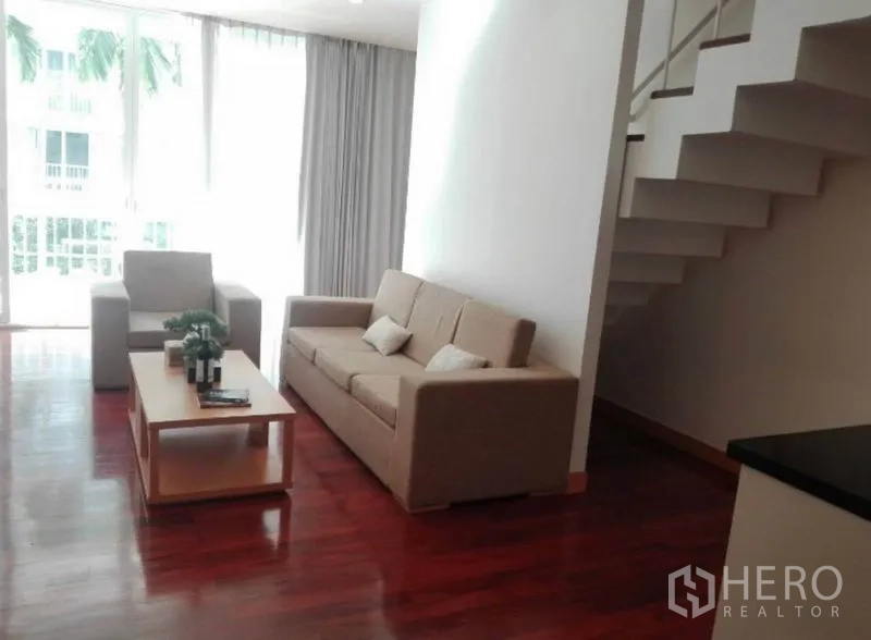 公寓 出租在Watthana, Bangkok - 客厅与开放式楼梯相邻，大面积玻璃引入自然光。