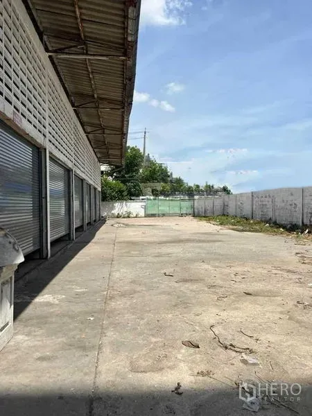 Warehouse for rent in Bang Na, Bangkok - Long loading driveway beside the warehouse with roller doors and boundary wall, offering ample truck maneuvering space.