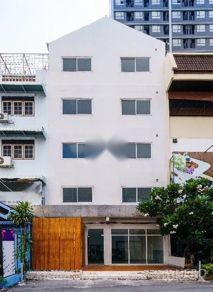 Home Office for rent in Khlong Toei, Bangkok - Four-storey white home office building with glass entry, wood feature wall and an urban streetscape backdrop.