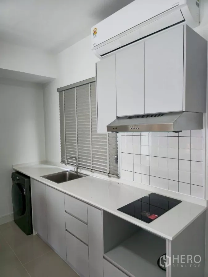 Townhouse for rent in Bang Phli, Samut Prakan - White linear kitchen with sink, electric cooktop, range hood, washer and window blinds.
