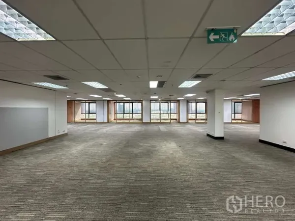 Office Space for rent in Khlong Toei, Bangkok - Large workspace with multiple windows, columns and emergency exit signage.