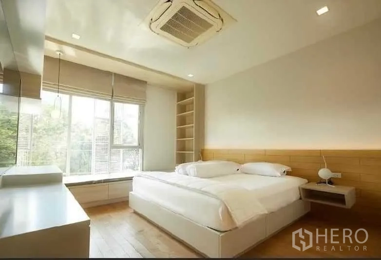 Townhouse for rent in Huai Khwang, Bangkok - Bright master bedroom with large window, wood flooring, built-in shelving and neutral decor.