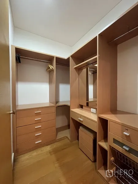 Condominium for rent or sale in Watthana, Bangkok - Walk-in closet with custom wood cabinetry, drawers, hanging rails, and a vanity mirror.