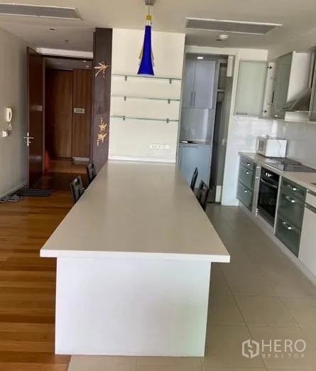 Condominium for rent in Khlong Toei, Bangkok - Modern kitchen with a long white island, pendant light, and built-in appliances.
