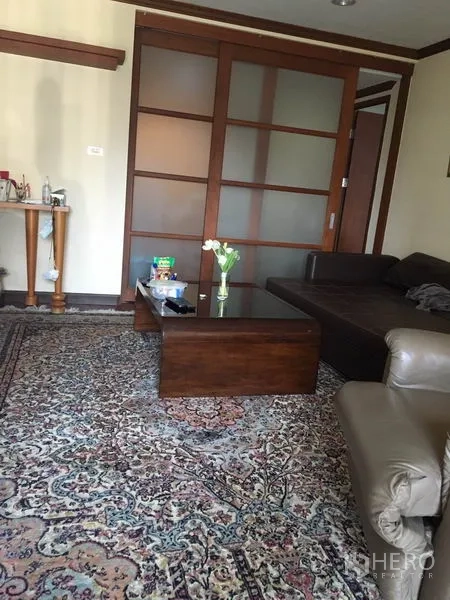 Condominium for rent or sale in Watthana, Bangkok - Living area with patterned rug, sectional sofa and sliding wooden doors.