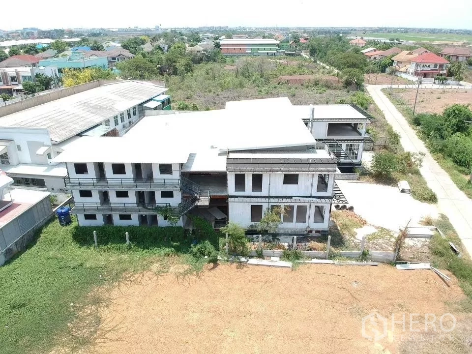 Land for sale in Phra Nakhon Si Ayutthaya, Phra Nakhon Si Ayutthaya - Drone view of a large land plot in Khlong Suan Plu with an unfinished multi‑storey building and open yard.