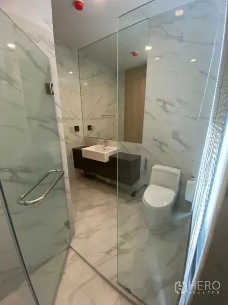 Condominium for rent in Watthana, Bangkok - Marble-tiled bathroom with glass-enclosed shower, toilet and sink.