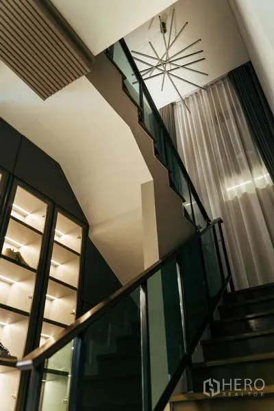 Detached House for sale in Sai Mai, Bangkok - Modern staircase with glass balustrade, tall curtains and a lit display cabinet beneath a chandelier.