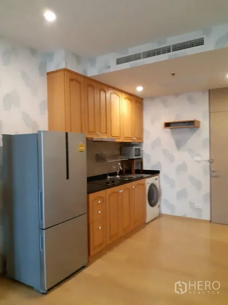 Condominium for rent in Phaya Thai, Bangkok - Compact kitchen with wooden cabinets, black countertop, sink, microwave, washing machine, and fridge.