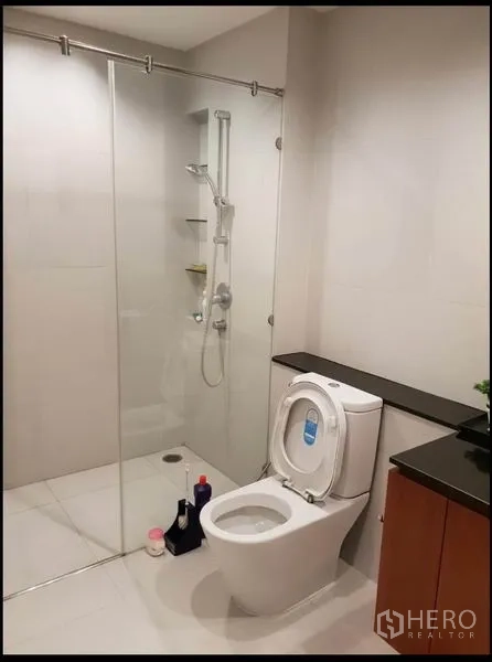 Condominium for rent in Sathon, Bangkok - Modern bathroom with glass-enclosed shower, toilet and stone vanity.