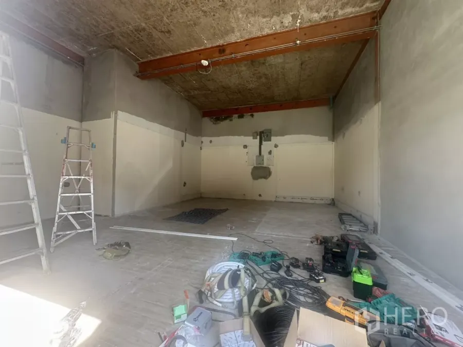 零售空间 出租在Bang Na, Bangkok - 毛坯零售铺面正在翻修，挑高天花与钢梁，地面散放梯子和工具，开间布局。