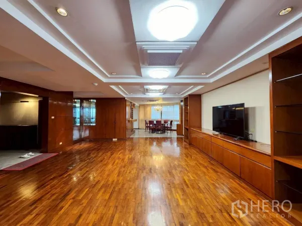 Condominium for rent in Khlong Toei, Bangkok - Open-plan lounge facing the dining area, timber cabinetry and layered ceiling lighting over glossy wood flooring.