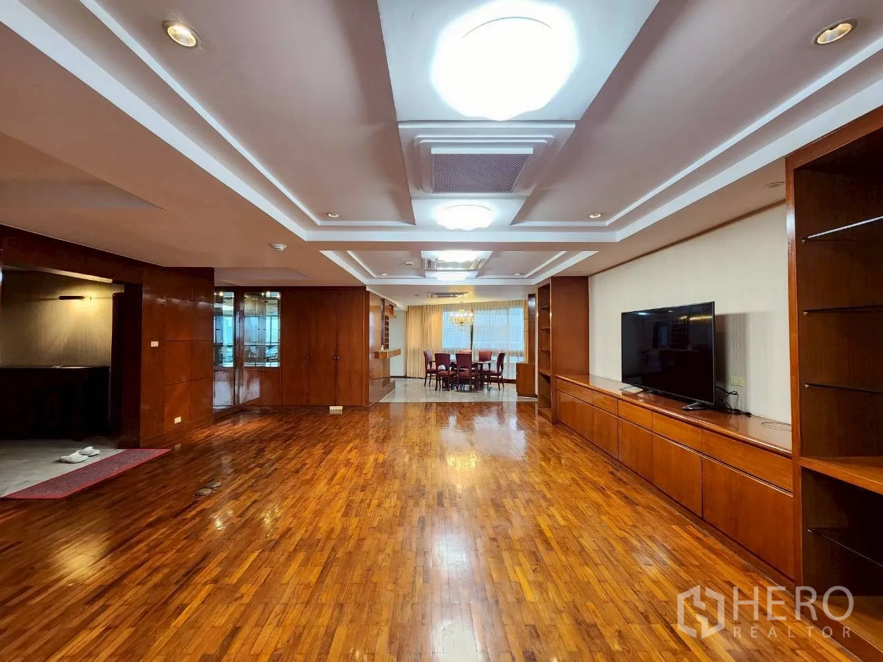Condominium for rent in Khlong Toei, Bangkok - Open-plan lounge facing the dining area, timber cabinetry and layered ceiling lighting over glossy wood flooring.