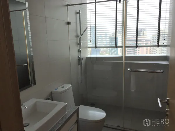 公寓 出租在Khlong Toei, Bangkok - 现代卫浴，玻璃淋浴间、台盆与面向天际线的窗户。