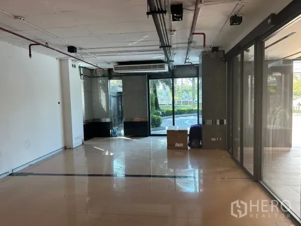 Office Space for rent in Khlong Toei, Bangkok - Open-plan office area with polished tile flooring, exposed ceiling services and sliding glass doors overlooking greenery.