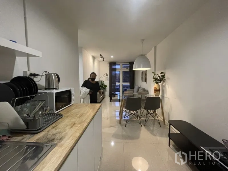Home Office for rent or sale in Watthana, Bangkok - Open-plan kitchenette with countertop and sink beside a dining set leading to a windowed living area.