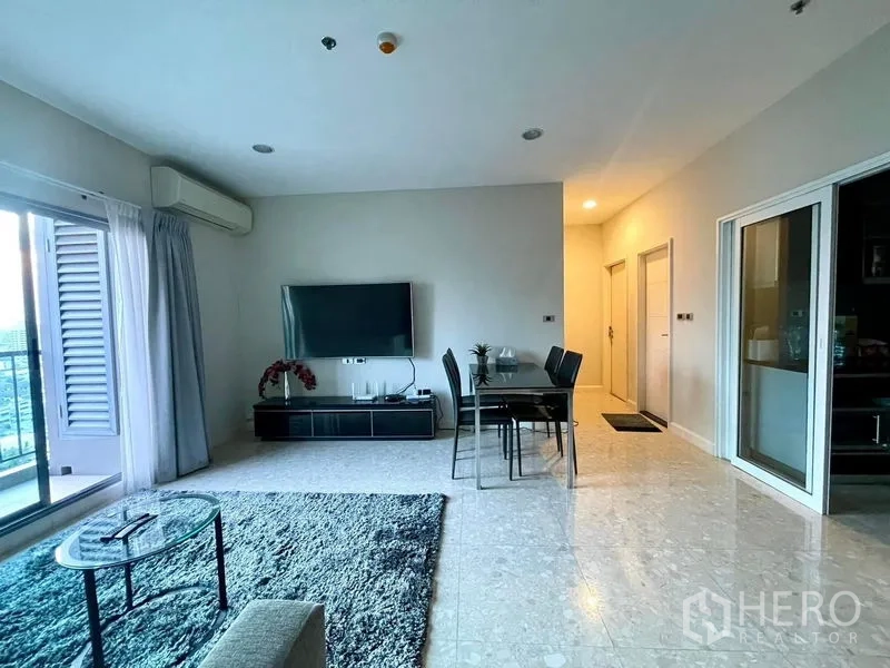 Condominium for sale in Khlong Toei, Bangkok - Bright living room with sliding balcony doors, wall-mounted TV, dining set and gray rug.