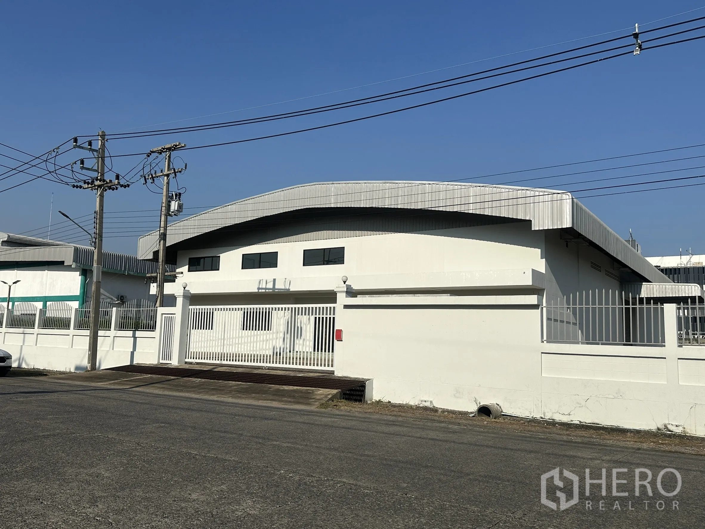 Factory for sale in Khlong Luang, Pathum Thani - Street view of a white factory with curved metal roof and gated entrance.